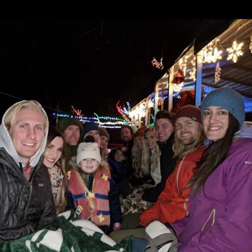 A group of people, including children, sitting together outdoors, surrounded by festive lights and decorations.
