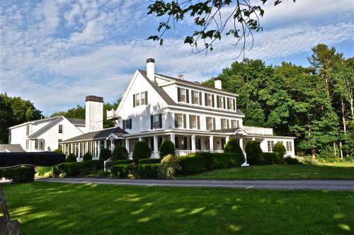 A large white house with multiple stories, surrounded by green trees and a well-maintained lawn under a blue sky.