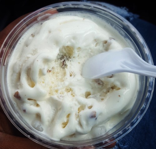 A close-up of a cup of creamy ice cream with a spoon, showing a partially eaten dessert.