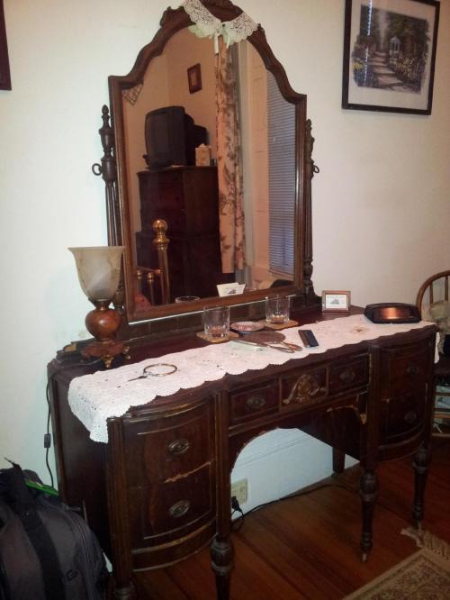 A vintage wooden dresser with a mirror, lace tablecloth, and decorative items in a cozy room.