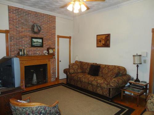 Cozy living room with a brick fireplace, patterned sofa, and wooden accents, featuring a ceiling fan and a rug.