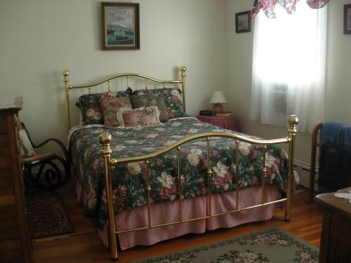 A cozy bedroom featuring a brass bed with floral bedding, a nightstand, and soft natural light from a window.