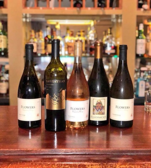 Five bottles of wine on a wooden bar, featuring labels from Flowers, Leviathan, and Illumination.
