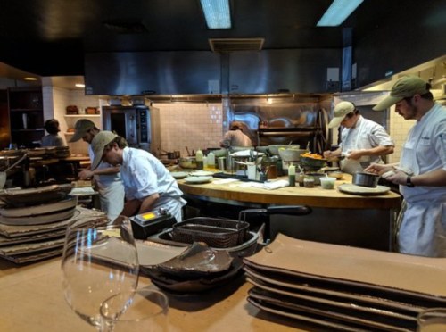 A busy restaurant kitchen with chefs preparing dishes, surrounded by cooking equipment and plates.