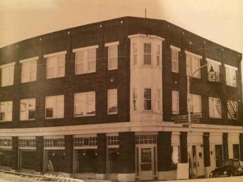 Historic black-and-white photo of a three-story brick building with multiple windows and a corner entrance.