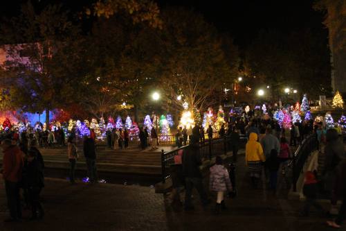 A festive night scene with colorful, illuminated Christmas trees and crowds of people enjoying the holiday atmosphere.