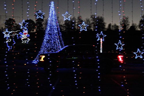A truck is parked in front of a brightly lit Christmas tree and star decorations, creating a festive nighttime scene.