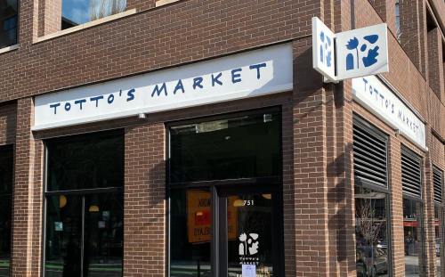 Exterior of Totto's Market, featuring a brick facade and a sign with the market's name and logo.