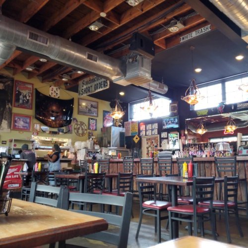 A cozy diner interior with wooden beams, tables, and eclectic decor, featuring a bar and patrons enjoying their meals.