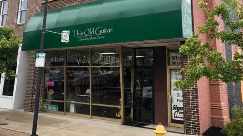 Storefront of "This Old Guitar," featuring a green awning and large windows displaying musical instruments and an open sign.