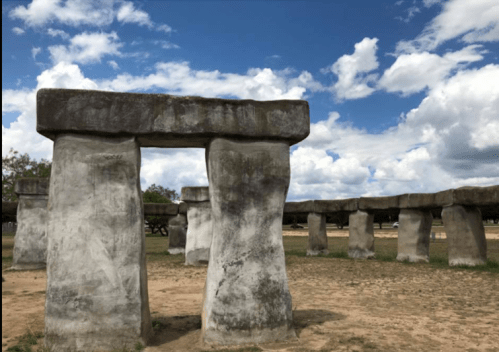 A replica of Stonehenge with large stone pillars under a cloudy blue sky.