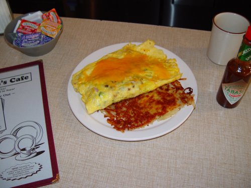 A plate with a cheese omelet and crispy hash browns, accompanied by condiments and a coffee cup in the background.