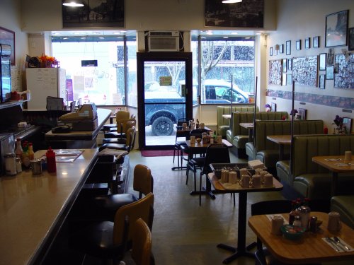A cozy diner interior with green booths, a counter, and large windows showing a snowy street outside.