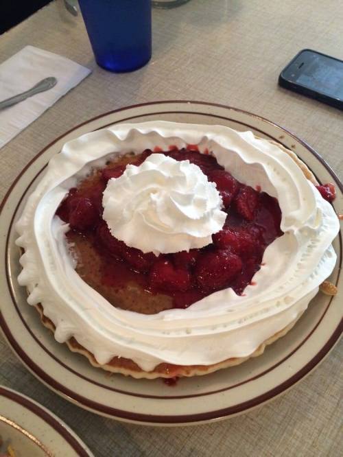 A large pancake topped with strawberries and a generous swirl of whipped cream on a plate.