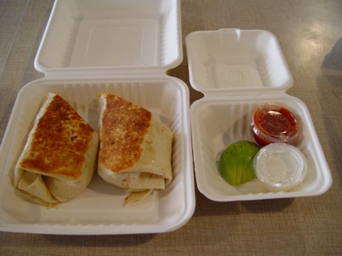 Two toasted burritos in a takeout container, accompanied by sauces and a small portion of guacamole.
