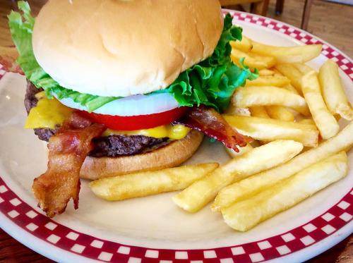 A juicy burger with lettuce, tomato, onion, cheese, and bacon, served with a side of golden French fries.
