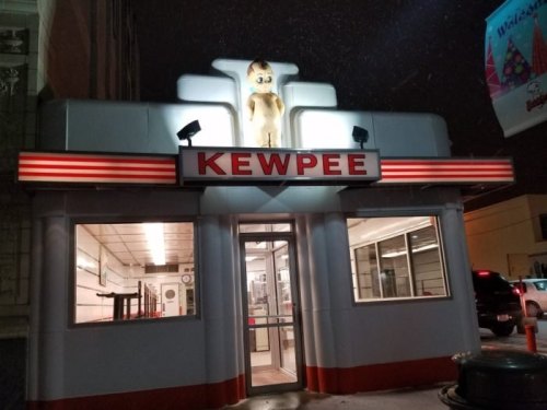 A retro diner named Kewpee with a large cartoon figure on the roof, illuminated at night during snowfall.