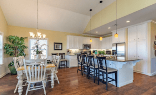 Bright, modern kitchen and dining area with white cabinets, wooden floors, and a large table surrounded by chairs.