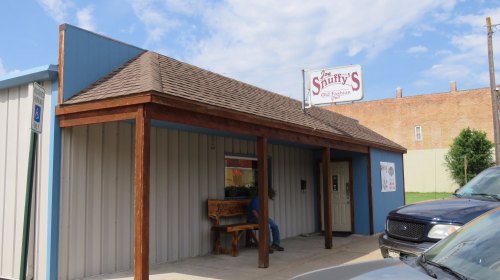 A small, one-story building with a wooden porch and a sign reading "Snuffy's Old Fashion." Cars parked nearby.