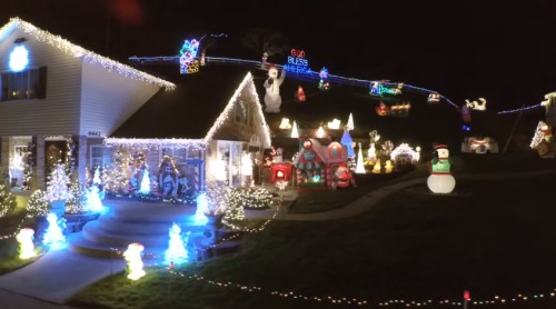 A brightly lit house decorated with colorful Christmas lights and festive inflatable decorations in a nighttime setting.