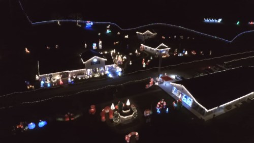 Aerial view of a festive display with colorful Christmas lights and decorations illuminating houses and yards at night.