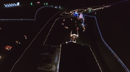 Aerial view of a festive light display along a winding path, featuring colorful decorations and parked cars.