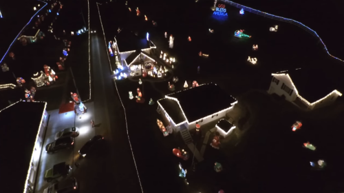 Aerial view of a neighborhood decorated with colorful Christmas lights and festive displays at night.