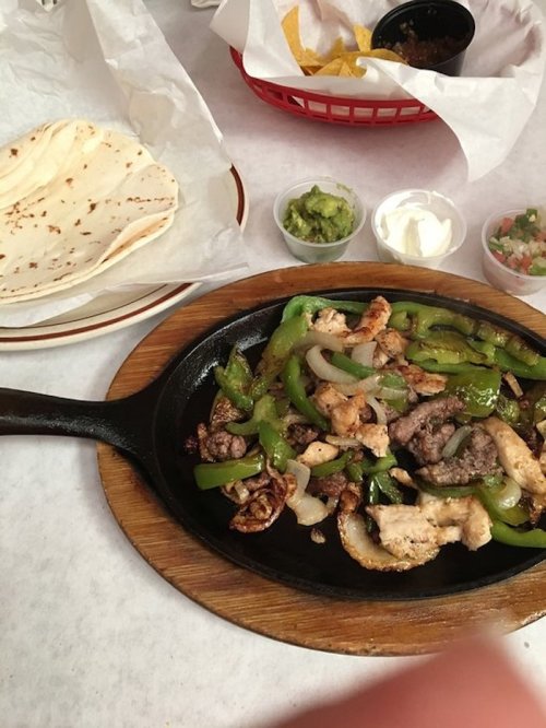 Sizzling fajitas on a skillet with grilled meat, peppers, onions, and sides of tortillas, guacamole, sour cream, and pico de gallo.