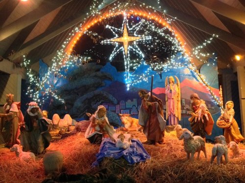 Nativity scene with figures of Mary, Joseph, baby Jesus, angels, and animals, surrounded by lights and a star.