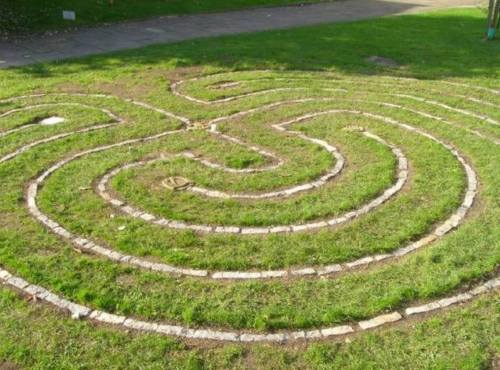 A grassy area featuring a spiral labyrinth made of stone pathways.