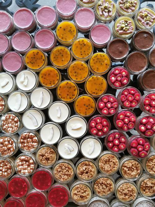 A colorful array of desserts in jars, featuring various flavors like passion fruit, coconut, and berry.