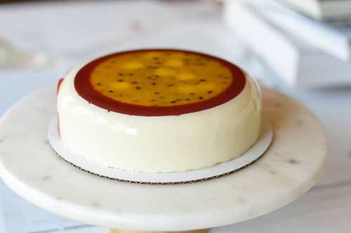 A round, glossy cake with a yellow and red glaze, displayed on a marble cake stand.