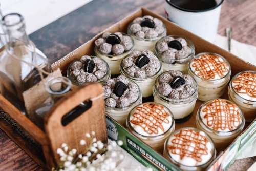 A box of assorted desserts in jars, topped with cookies and caramel, alongside a cup of coffee and decorative elements.