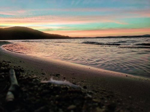 A serene beach at sunset, with gentle waves lapping at the shore and colorful skies reflecting over the water.