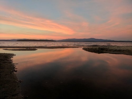 A serene landscape at sunset, featuring calm water reflecting colorful skies and distant mountains.