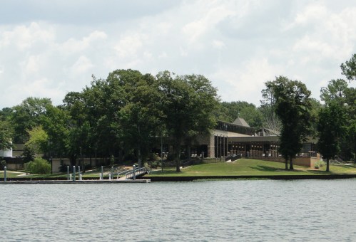 A serene lakeside view featuring a building surrounded by trees and a dock along the water's edge.
