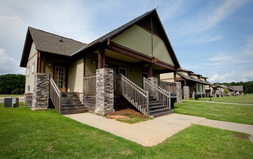 A row of two-story houses with stone steps and porches, set on a grassy area under a blue sky.