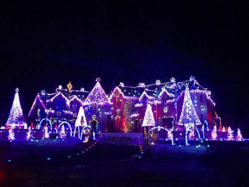 A brightly lit house decorated with colorful Christmas lights and festive trees, glowing against a dark night sky.