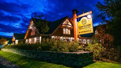 A cozy building at dusk with a sign reading "Lawson's Finest Liquids" and lush greenery surrounding it.