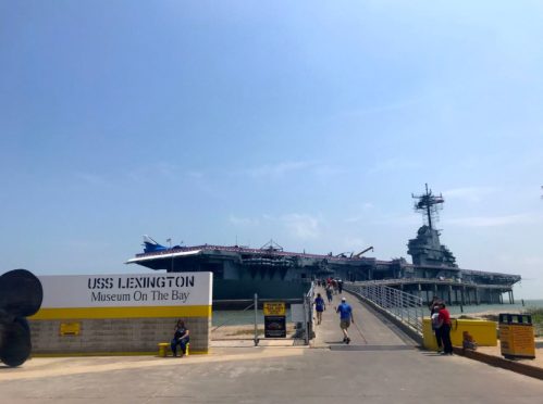 Visitors approach the USS Lexington Museum on the Bay, a historic aircraft carrier, under a clear blue sky.