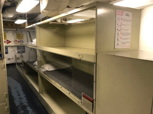Interior of a ship's bunk room with empty shelves and pillows, featuring a clean, organized layout.
