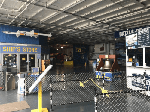 Interior of a museum store with displays, a ticket counter, and a military aircraft in the background.