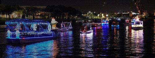 Colorful boats decorated with lights and holiday themes float on a dark waterway at night.