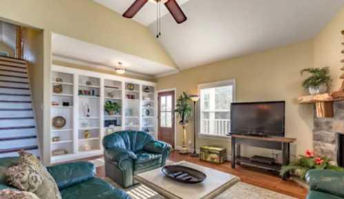 Cozy living room with green leather furniture, a TV, built-in shelves, and a staircase in a warm, inviting space.