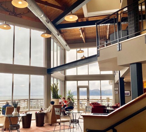 Cozy interior of a modern café with large windows, showcasing a view of the ocean and people enjoying their time.