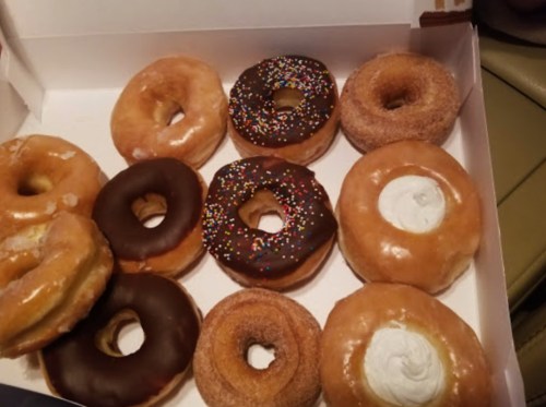 A box of assorted donuts, including glazed, chocolate, and sprinkled varieties, arranged neatly.