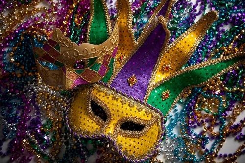 Colorful Mardi Gras masks and beads in purple, green, and gold, arranged artistically on a surface.