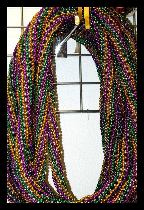 Colorful strands of Mardi Gras beads in purple, green, and gold hanging on a display.