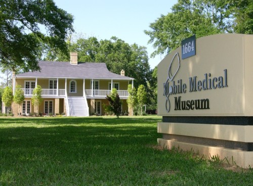 A historic building with a sign for the Mobile Medical Museum, surrounded by green grass and trees.