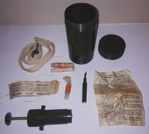 A collection of vintage medical supplies, including a black container, tape, a syringe, and instruction papers.